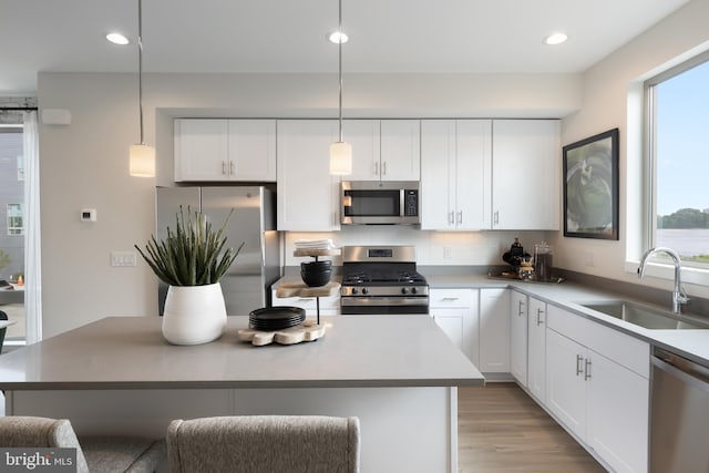 kitchen with light hardwood / wood-style flooring, appliances with stainless steel finishes, sink, white cabinets, and a kitchen island