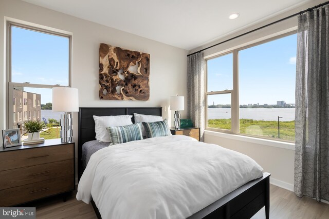 bedroom with light hardwood / wood-style flooring and a water view