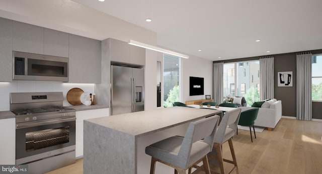 kitchen with light wood-type flooring, a breakfast bar area, gray cabinets, appliances with stainless steel finishes, and backsplash