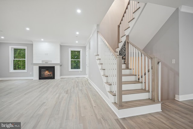 stairway with hardwood / wood-style flooring, ornamental molding, and a large fireplace