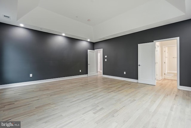 spare room featuring a tray ceiling and light wood-type flooring