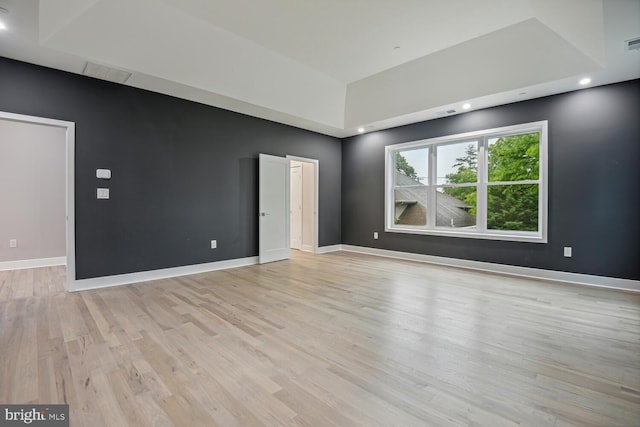 empty room with a tray ceiling and light hardwood / wood-style floors