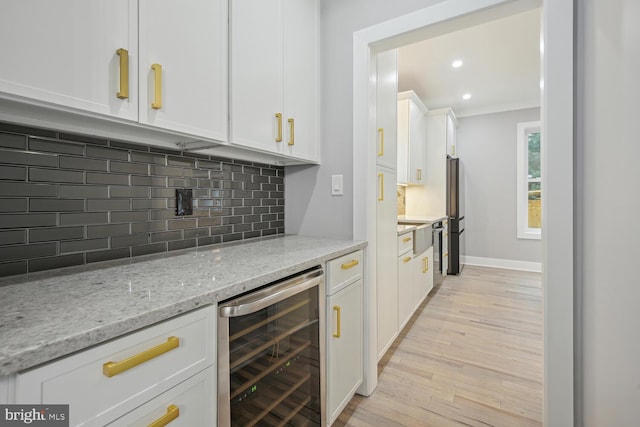 kitchen with white cabinets, beverage cooler, light stone countertops, light hardwood / wood-style floors, and backsplash