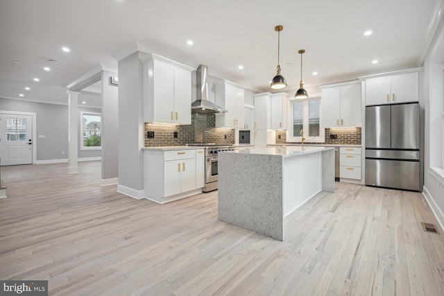 kitchen with white cabinets, appliances with stainless steel finishes, and wall chimney range hood