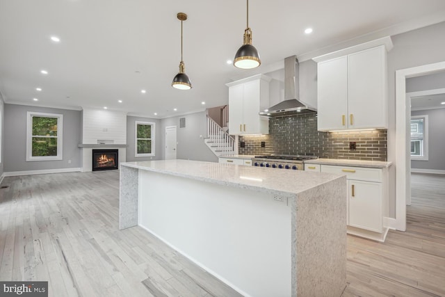 kitchen with stove, a center island, white cabinets, decorative light fixtures, and wall chimney exhaust hood