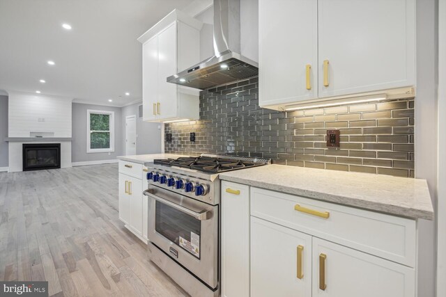 kitchen featuring tasteful backsplash, stainless steel range, wall chimney range hood, light stone countertops, and white cabinets