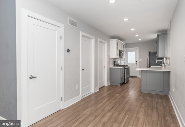 kitchen featuring kitchen peninsula, backsplash, stainless steel appliances, dark wood-type flooring, and gray cabinets