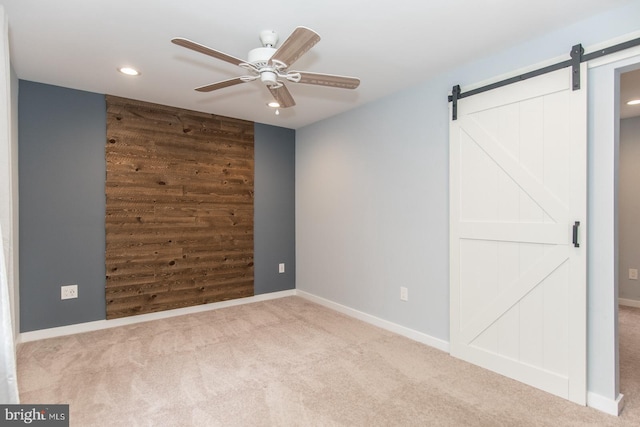 carpeted empty room featuring a barn door, wood walls, and ceiling fan