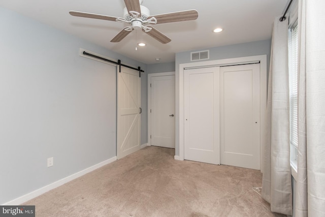 unfurnished bedroom featuring a closet, a barn door, light colored carpet, and ceiling fan