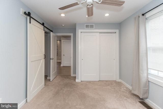 unfurnished bedroom featuring a barn door, light carpet, a closet, and multiple windows