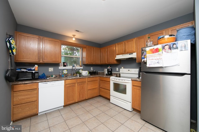 kitchen featuring white appliances, dark stone counters, light tile patterned flooring, and sink