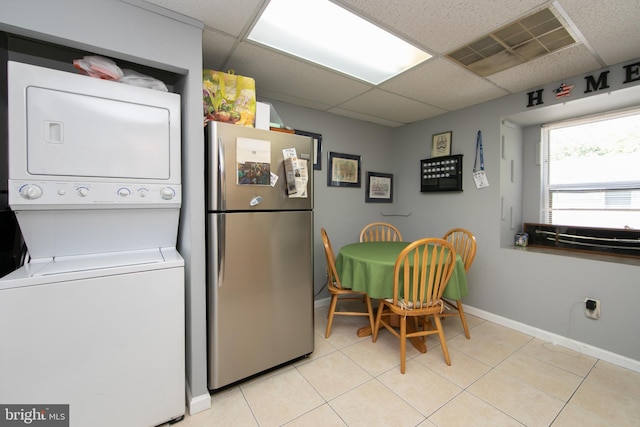 kitchen featuring stainless steel fridge, light tile patterned floors, stacked washer and clothes dryer, and a drop ceiling