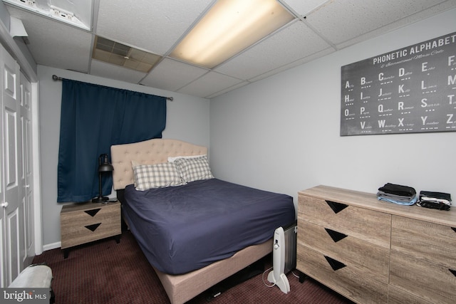 bedroom with a closet, dark carpet, and a drop ceiling