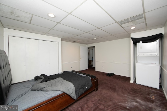 carpeted bedroom with stacked washer and clothes dryer and a drop ceiling