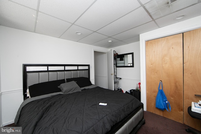 carpeted bedroom with a closet and a paneled ceiling