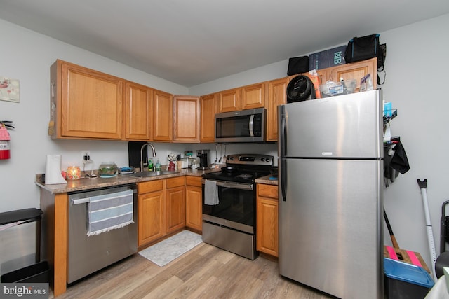 kitchen featuring dark stone countertops, sink, appliances with stainless steel finishes, and light hardwood / wood-style floors