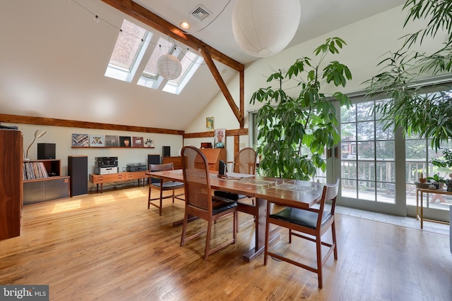 dining space featuring high vaulted ceiling, a skylight, beam ceiling, and light hardwood / wood-style floors