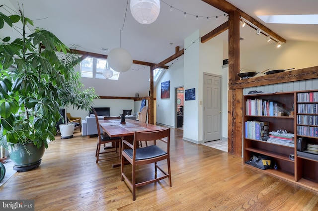 dining area with beamed ceiling, light wood-type flooring, high vaulted ceiling, and rail lighting