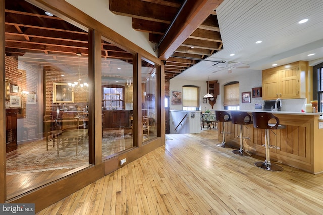 kitchen featuring light wood-type flooring, ceiling fan with notable chandelier, pendant lighting, kitchen peninsula, and brick wall