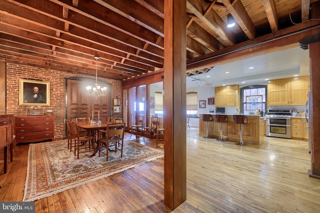 dining area with ceiling fan with notable chandelier, light hardwood / wood-style floors, and brick wall