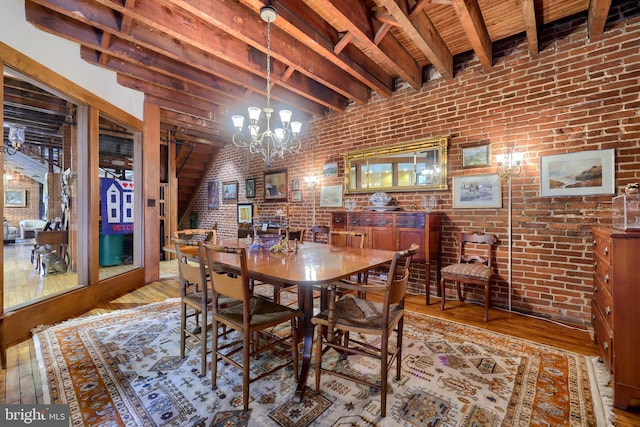 dining room featuring light hardwood / wood-style flooring, brick wall, beamed ceiling, and an inviting chandelier