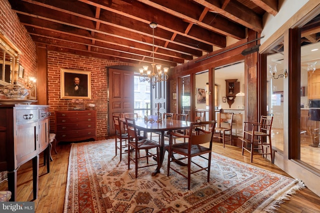 dining area with light wood-type flooring, a chandelier, brick wall, and beamed ceiling