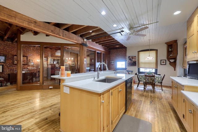 kitchen with beamed ceiling, a kitchen island with sink, brick wall, and sink