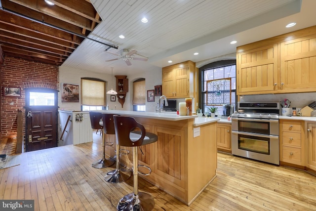 kitchen with ceiling fan, brick wall, a kitchen breakfast bar, double oven range, and light hardwood / wood-style floors