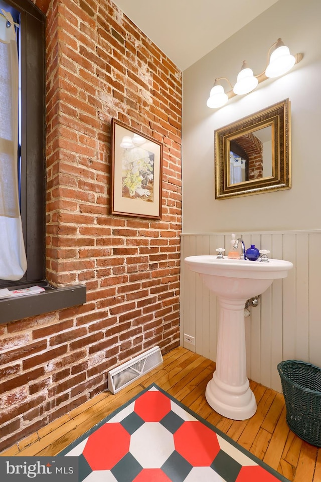 bathroom with hardwood / wood-style flooring and brick wall