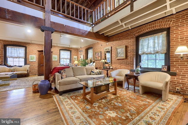 living room featuring wood-type flooring, brick wall, and a high ceiling