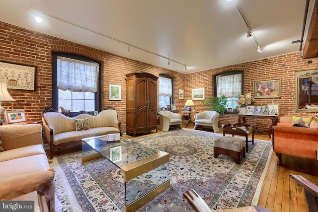 living room with brick wall, hardwood / wood-style floors, and rail lighting