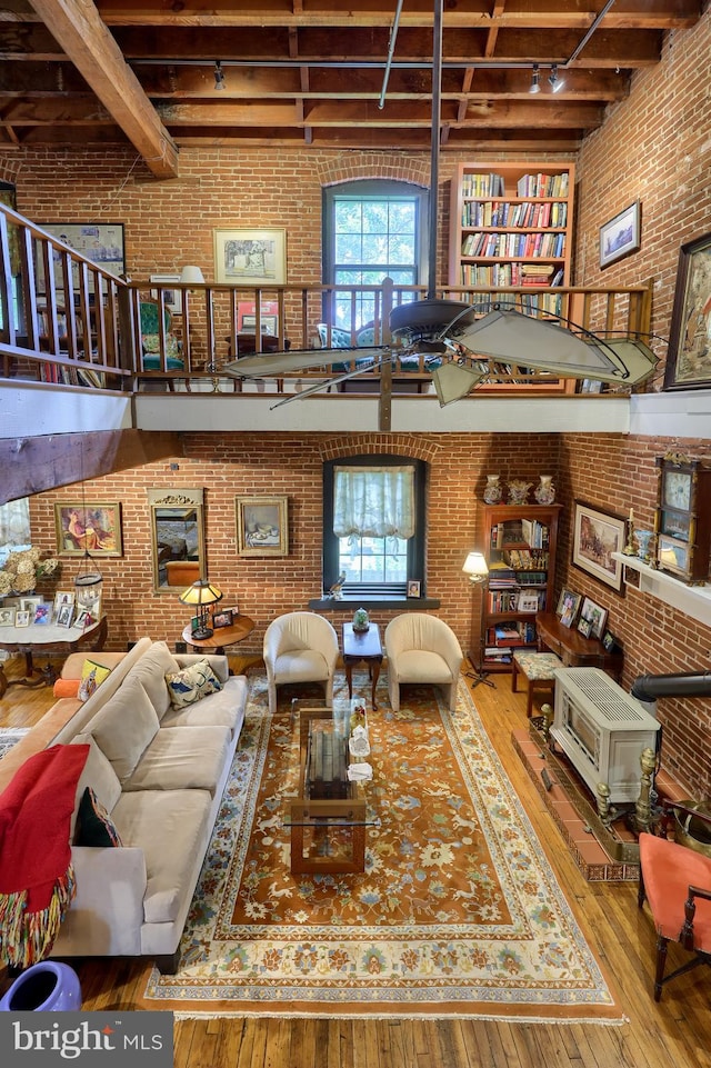 living room featuring wood-type flooring, beam ceiling, track lighting, and brick wall