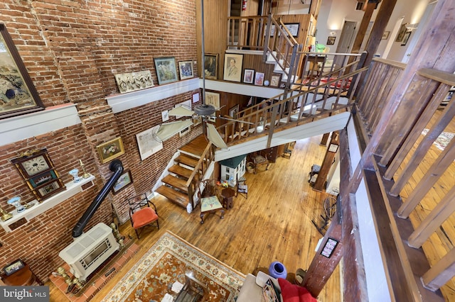 living room featuring ceiling fan, a towering ceiling, hardwood / wood-style floors, and brick wall