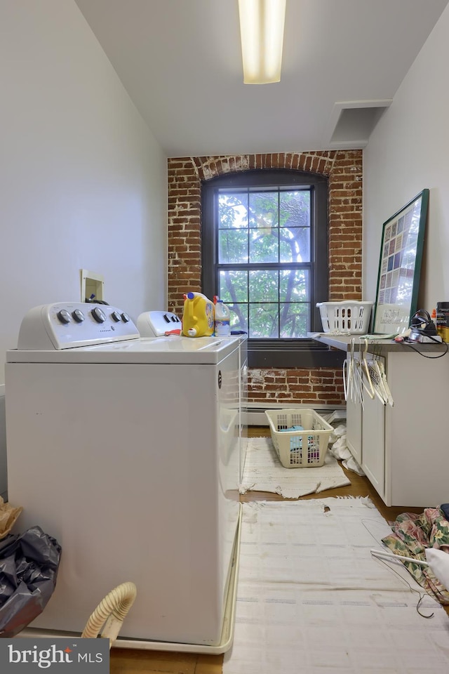 clothes washing area with brick wall, light hardwood / wood-style flooring, and washer and clothes dryer