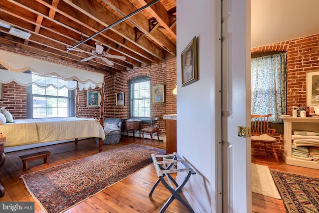 bedroom with baseboard heating, light hardwood / wood-style flooring, beam ceiling, and brick wall