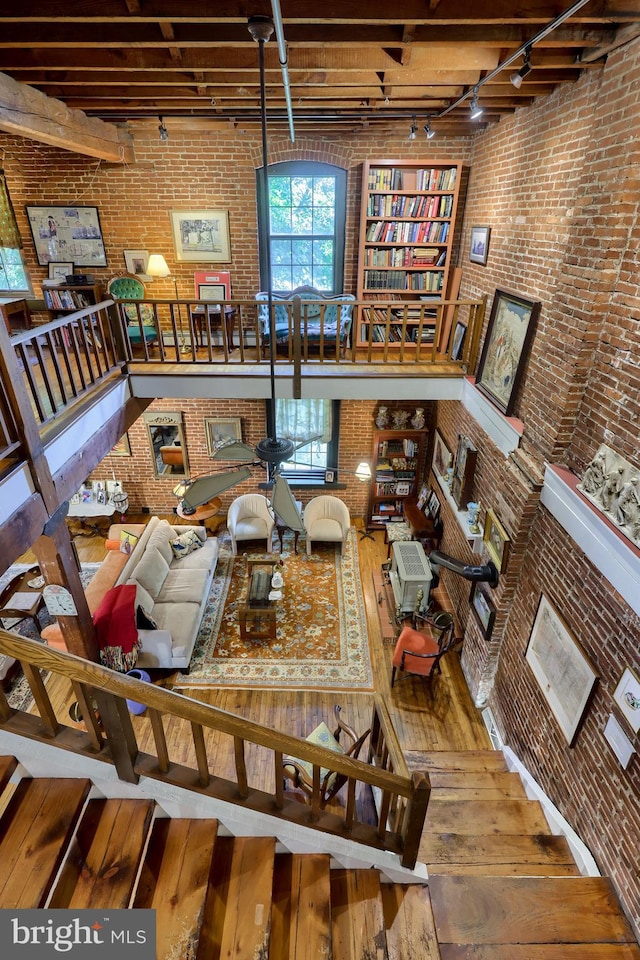 living room featuring rail lighting, brick wall, wood-type flooring, and a high ceiling