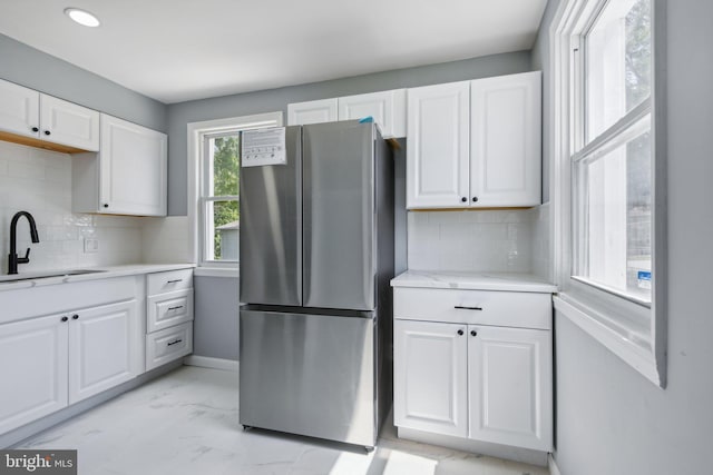 kitchen featuring sink, decorative backsplash, stainless steel refrigerator, light tile patterned floors, and white cabinets