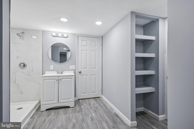 bathroom featuring wood-type flooring, vanity, a tile shower, and built in shelves