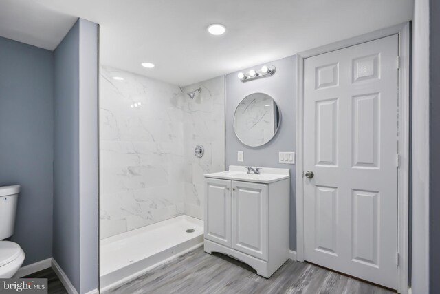 bathroom with toilet, hardwood / wood-style floors, vanity, and a tile shower