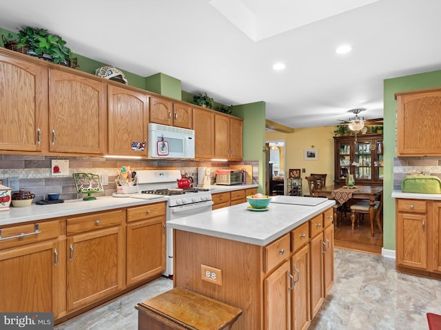 kitchen featuring white appliances, ceiling fan, a kitchen island, and tasteful backsplash