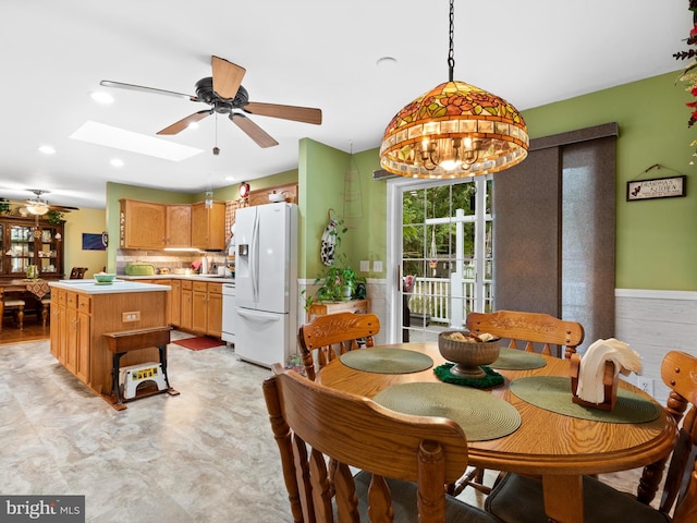 dining space with ceiling fan with notable chandelier and a skylight