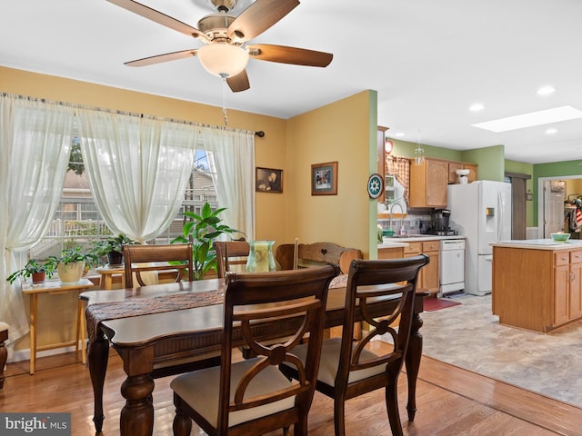 dining room featuring light hardwood / wood-style floors, sink, ceiling fan, and a skylight