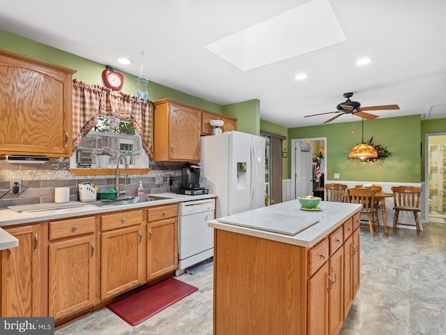 kitchen with white appliances, a kitchen island, ceiling fan, a skylight, and sink