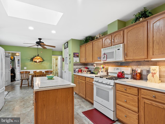 kitchen with a kitchen island, decorative backsplash, white appliances, a skylight, and ceiling fan