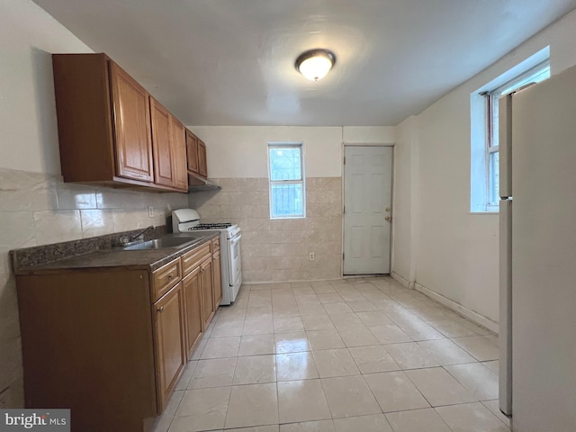 kitchen with light tile patterned flooring, white appliances, sink, and tile walls