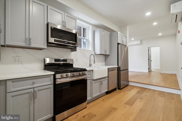 kitchen featuring stainless steel appliances, sink, tasteful backsplash, light hardwood / wood-style floors, and gray cabinetry