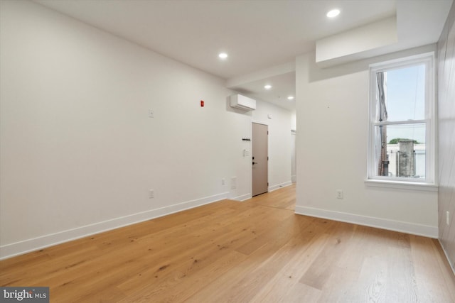 unfurnished room featuring an AC wall unit, plenty of natural light, and light hardwood / wood-style floors