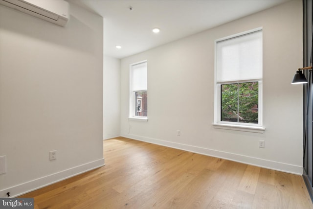 spare room with light wood-type flooring, a wall unit AC, and a healthy amount of sunlight