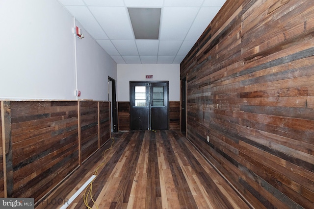 hallway with dark hardwood / wood-style floors, wooden walls, and a drop ceiling