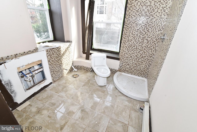 bathroom featuring tiled shower, toilet, and a baseboard heating unit